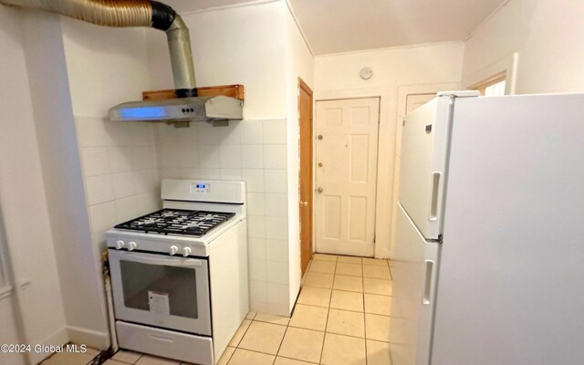 kitchen with tasteful backsplash, white refrigerator, light tile patterned flooring, and stainless steel gas range oven