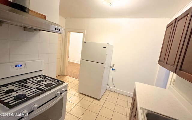 kitchen featuring wall chimney exhaust hood, white refrigerator, tile walls, gas range, and light tile patterned floors