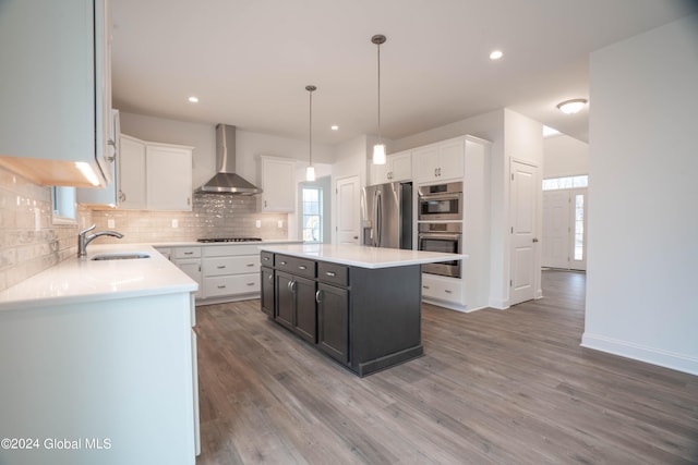 kitchen with appliances with stainless steel finishes, wall chimney exhaust hood, decorative backsplash, hardwood / wood-style flooring, and decorative light fixtures