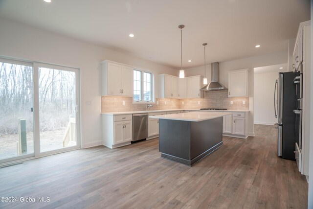 kitchen featuring wall chimney range hood, a kitchen island, appliances with stainless steel finishes, decorative backsplash, and wood-type flooring