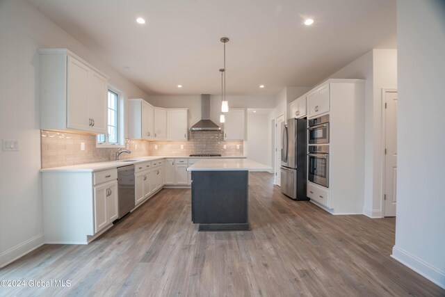 kitchen featuring white cabinets, backsplash, appliances with stainless steel finishes, wall chimney exhaust hood, and hardwood / wood-style flooring