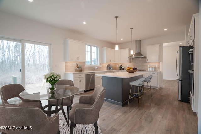 kitchen with white cabinetry, wall chimney range hood, backsplash, appliances with stainless steel finishes, and wood-type flooring