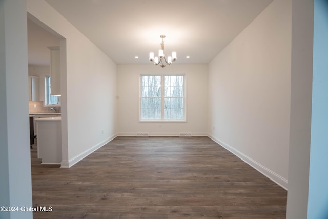 unfurnished dining area with dark wood-style flooring, visible vents, baseboards, and an inviting chandelier