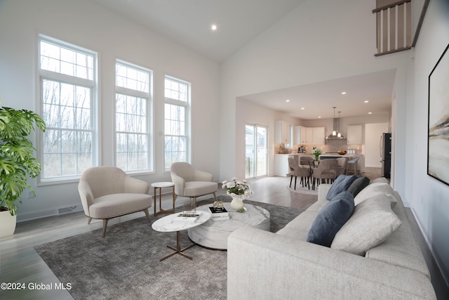 living area with baseboards, high vaulted ceiling, light wood finished floors, and recessed lighting