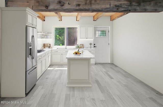 kitchen with beam ceiling, appliances with stainless steel finishes, a center island, and light hardwood / wood-style floors