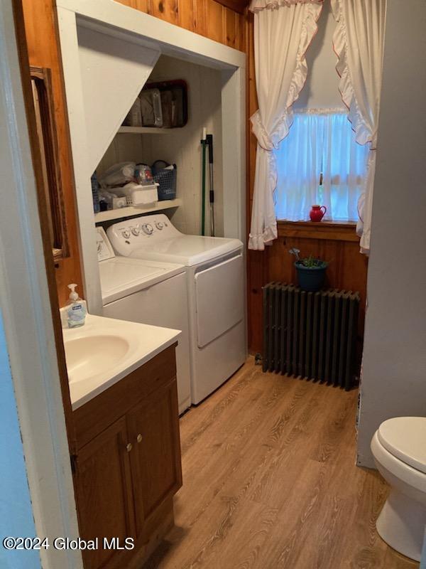 laundry room featuring radiator heating unit, light wood-type flooring, sink, and washer and dryer