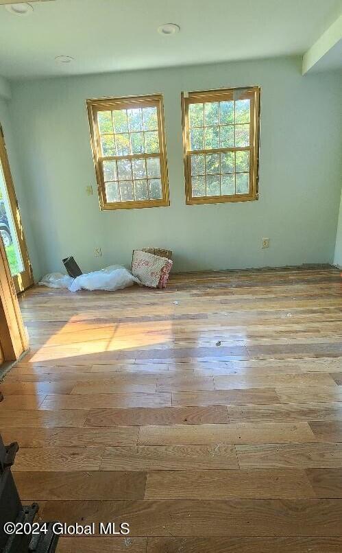 empty room with light hardwood / wood-style flooring, beam ceiling, and a healthy amount of sunlight