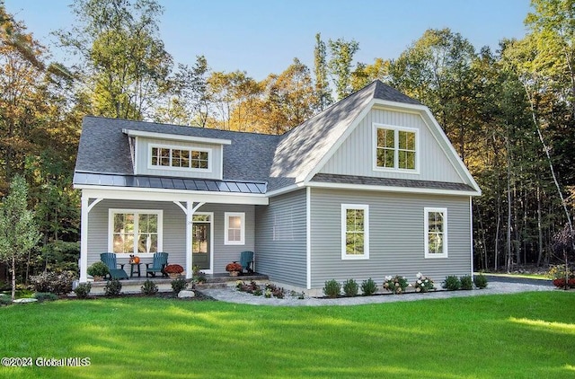 view of front facade featuring a standing seam roof, a porch, a shingled roof, a front lawn, and metal roof