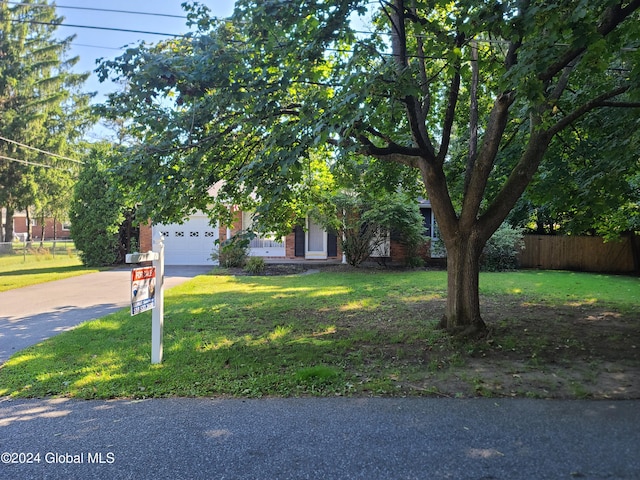 21 Foxhall Dr, Saratoga Springs, NY 12866 - view of property hidden behind natural elements featuring driveway, a front yard, fence, brick siding, and a garage