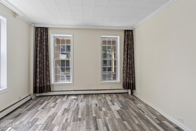 empty room with a baseboard heating unit, plenty of natural light, and light wood-type flooring