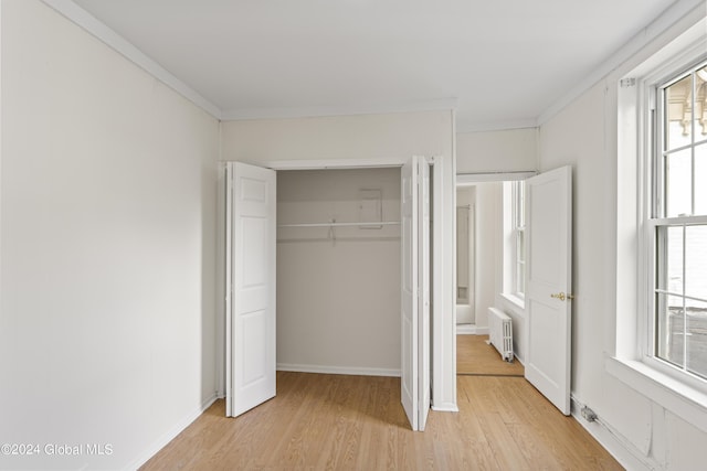 unfurnished bedroom featuring crown molding, radiator heating unit, light wood-type flooring, and a closet