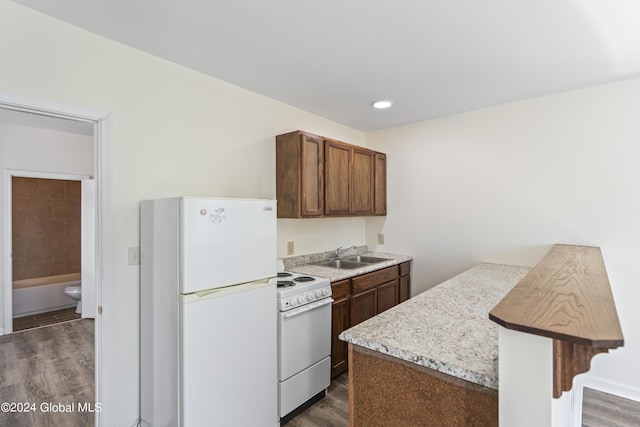 kitchen featuring sink, a kitchen breakfast bar, dark hardwood / wood-style flooring, light stone countertops, and white appliances