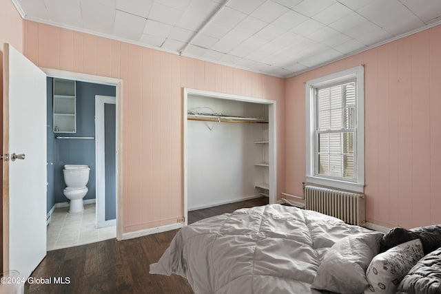 bedroom featuring dark wood-type flooring, radiator heating unit, crown molding, and a closet