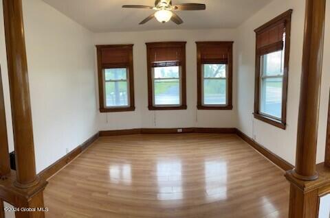 empty room featuring light hardwood / wood-style floors, ceiling fan, and ornate columns