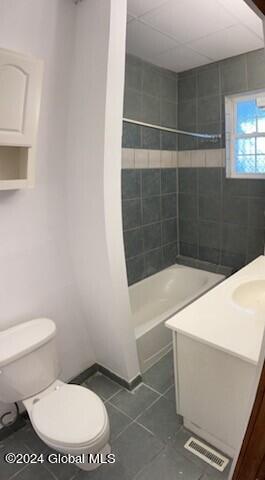 full bathroom featuring tile patterned flooring, toilet, tiled shower / bath, and vanity