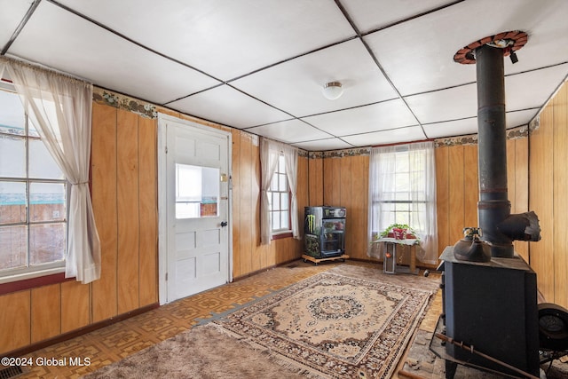 entrance foyer featuring parquet flooring, a drop ceiling, a wood stove, and wood walls