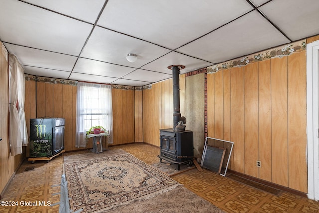 unfurnished living room featuring a paneled ceiling, parquet floors, a wood stove, and wooden walls