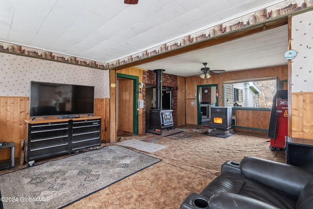 carpeted living room featuring ceiling fan, a wood stove, and wooden walls