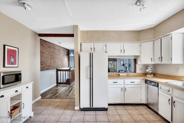 kitchen with brick wall, a textured ceiling, white cabinetry, and stainless steel appliances