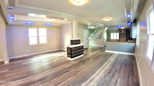 unfurnished living room featuring a raised ceiling, ornamental molding, and dark hardwood / wood-style floors