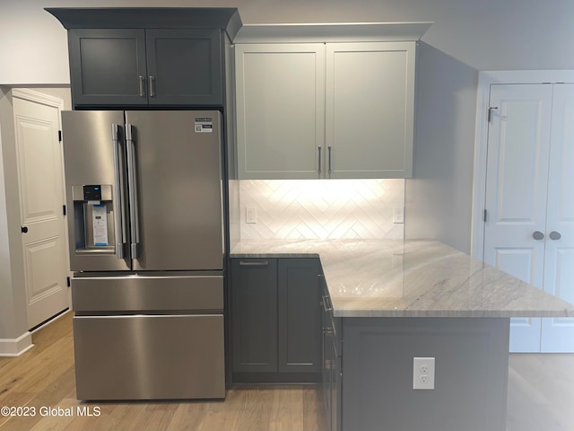 kitchen with backsplash, light wood-type flooring, light stone counters, stainless steel refrigerator with ice dispenser, and kitchen peninsula