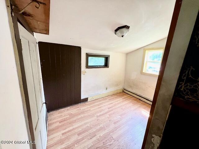 unfurnished bedroom featuring lofted ceiling, light hardwood / wood-style floors, and a baseboard heating unit