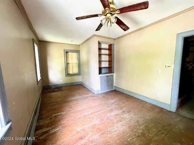 unfurnished bedroom with a baseboard radiator, wood-type flooring, ceiling fan, and crown molding