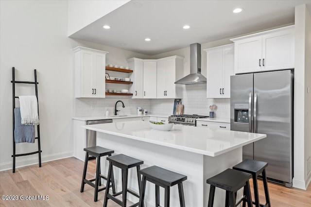 kitchen with a breakfast bar, a center island, light wood-type flooring, wall chimney exhaust hood, and stainless steel appliances