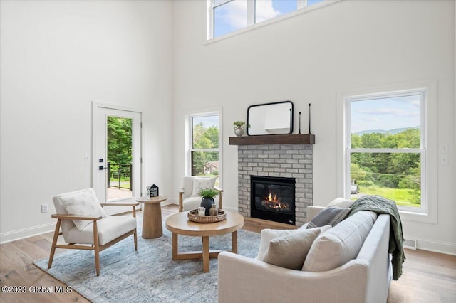 living room with a fireplace, light wood-type flooring, and a towering ceiling