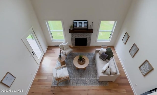 living room featuring a towering ceiling, light hardwood / wood-style flooring, and a brick fireplace