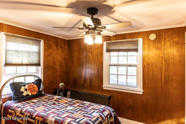 bedroom with ceiling fan, wooden walls, and ornamental molding