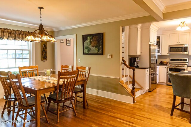 dining room featuring light wood-type flooring, ornamental molding, and a notable chandelier