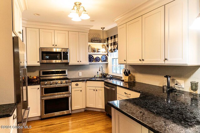 kitchen with pendant lighting, sink, stainless steel appliances, dark stone countertops, and light wood-type flooring