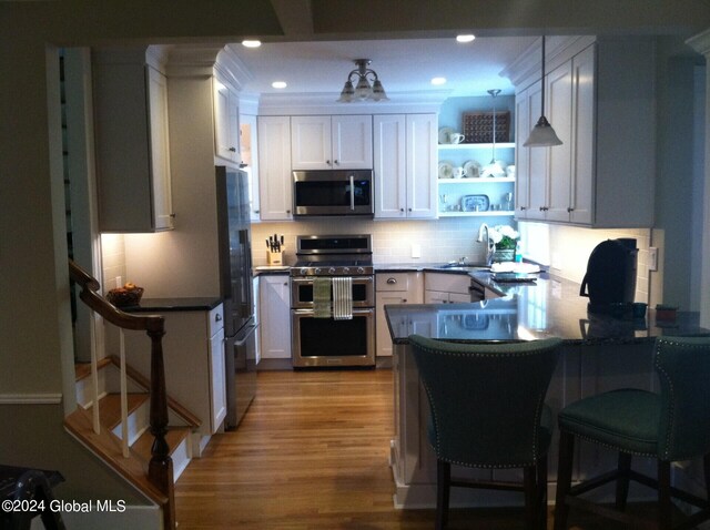 kitchen with light wood-type flooring, white cabinetry, kitchen peninsula, a kitchen breakfast bar, and appliances with stainless steel finishes