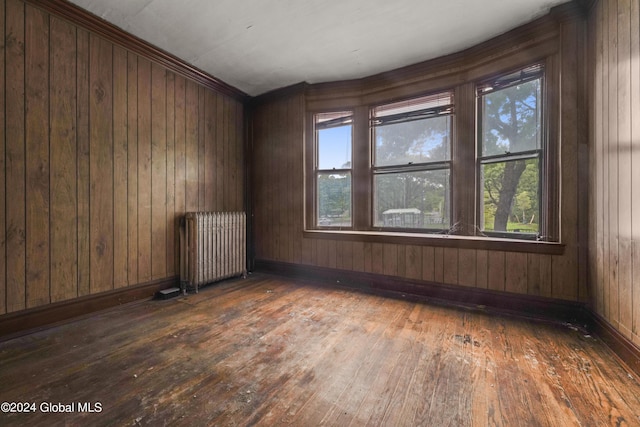 spare room with radiator, wood walls, baseboards, and hardwood / wood-style floors