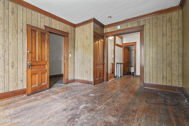 spare room with ornamental molding, wooden walls, baseboards, and hardwood / wood-style flooring