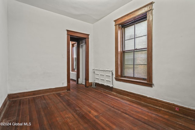 empty room with baseboards, hardwood / wood-style floors, and radiator heating unit