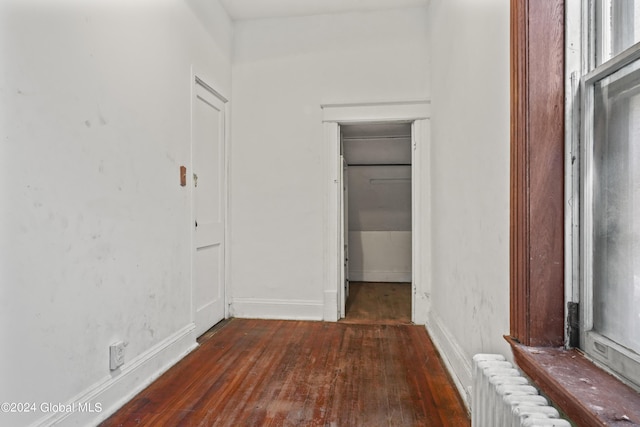 hallway with radiator heating unit, baseboards, and dark wood-style flooring