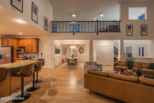 living room with a high ceiling, ornate columns, and light wood-type flooring