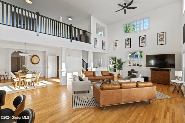 living room featuring decorative columns, light hardwood / wood-style floors, a towering ceiling, and ceiling fan