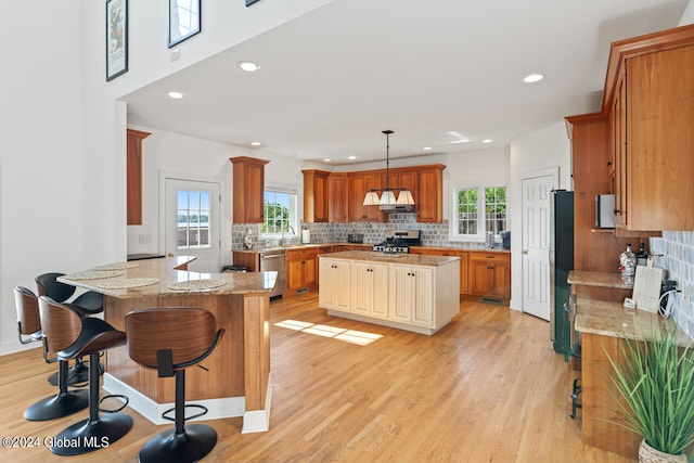 kitchen with light stone countertops, extractor fan, a kitchen island, stainless steel appliances, and hanging light fixtures