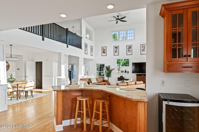 kitchen with light stone countertops, a kitchen bar, wine cooler, kitchen peninsula, and light hardwood / wood-style flooring