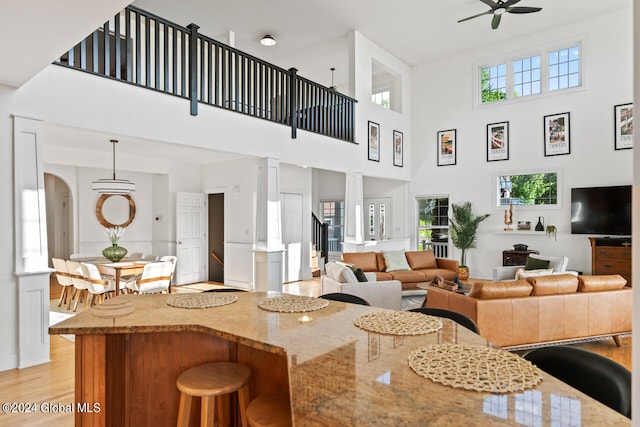 living room featuring light hardwood / wood-style floors, ceiling fan, a wealth of natural light, and a towering ceiling