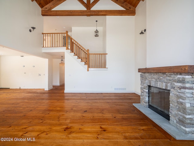 unfurnished living room with a stone fireplace, hardwood / wood-style flooring, beamed ceiling, and high vaulted ceiling