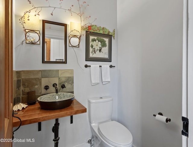 half bath featuring backsplash, toilet, and a sink