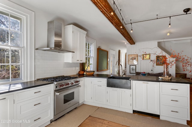 kitchen featuring dark countertops, a sink, premium range, and wall chimney range hood