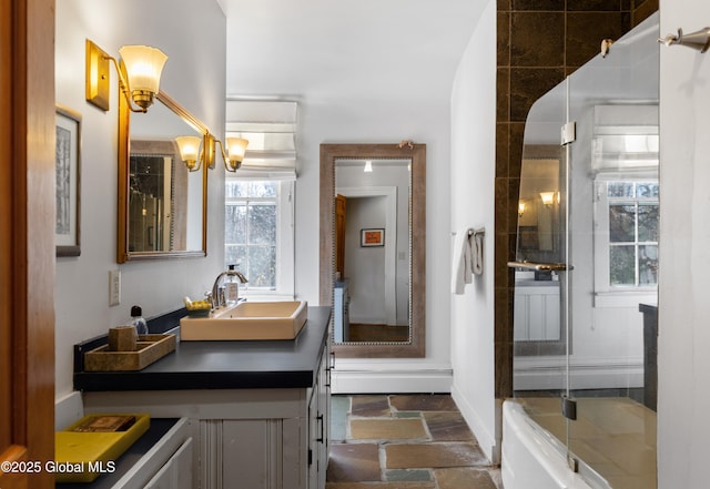 full bathroom featuring baseboards, stone tile flooring, vanity, and a shower with shower door