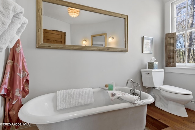 full bathroom with toilet, a freestanding tub, and wood finished floors