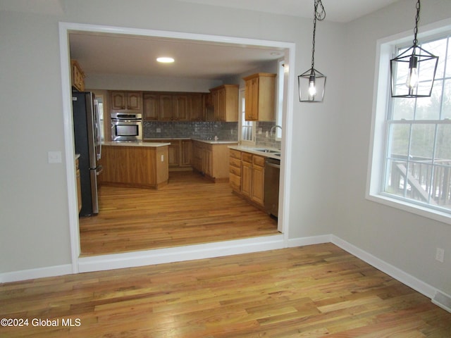 kitchen with light wood-type flooring, tasteful backsplash, sink, appliances with stainless steel finishes, and decorative light fixtures