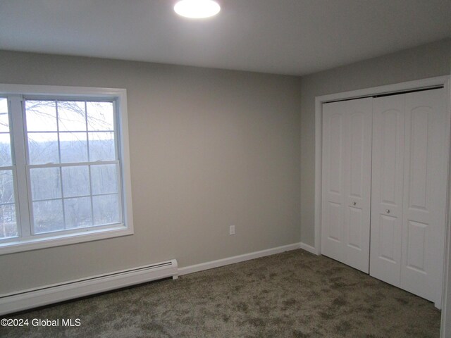 unfurnished bedroom with baseboard heating, dark carpet, and a closet